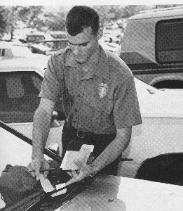 Officer putting parking ticket under windshield wiper.