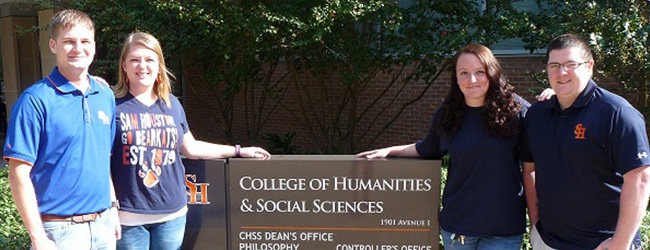Four students stand by the sign for the College of Humanities and Social Sciences building.