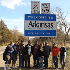 Photograph in front of Arkansas state sign for section named Spring Break Service