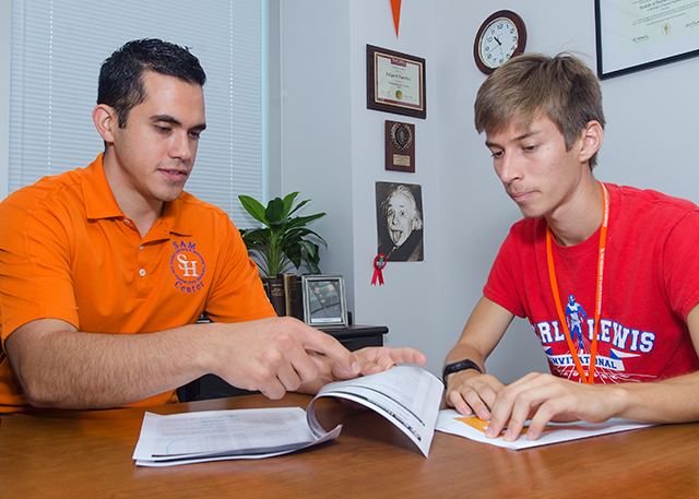 An advisor and student sit at a desk and review a degree plan.