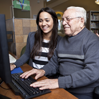 Older gentlemen at a computer while a young adult helps him