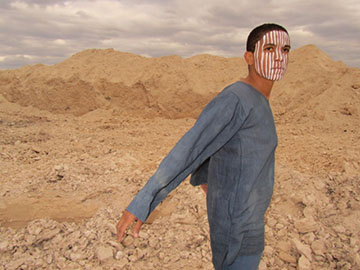 A man with a painted face stands in a desert setting.