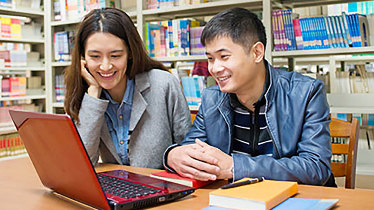 Two Students in a library looking at a laptop computer.
