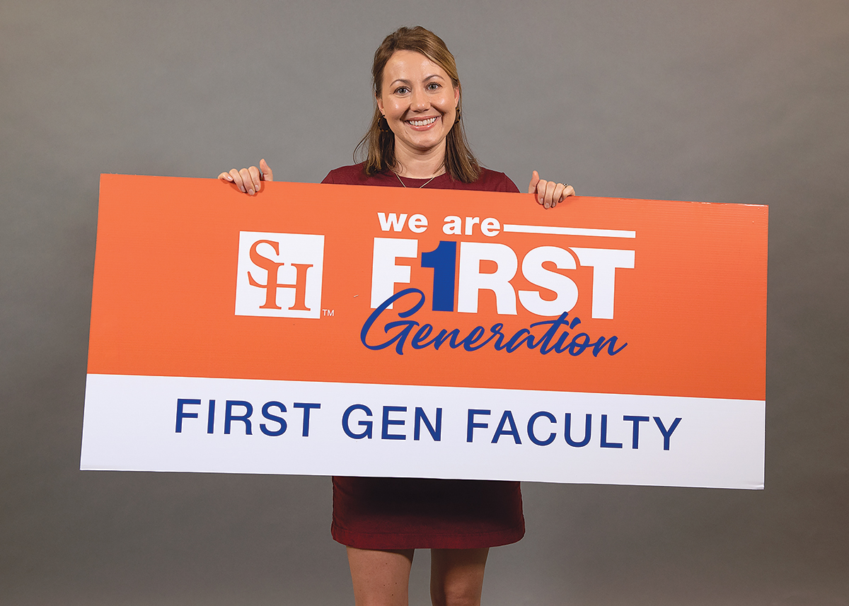 Dr. April O'brien holds up a sign that says We Are First Generation - First Gen Faculty