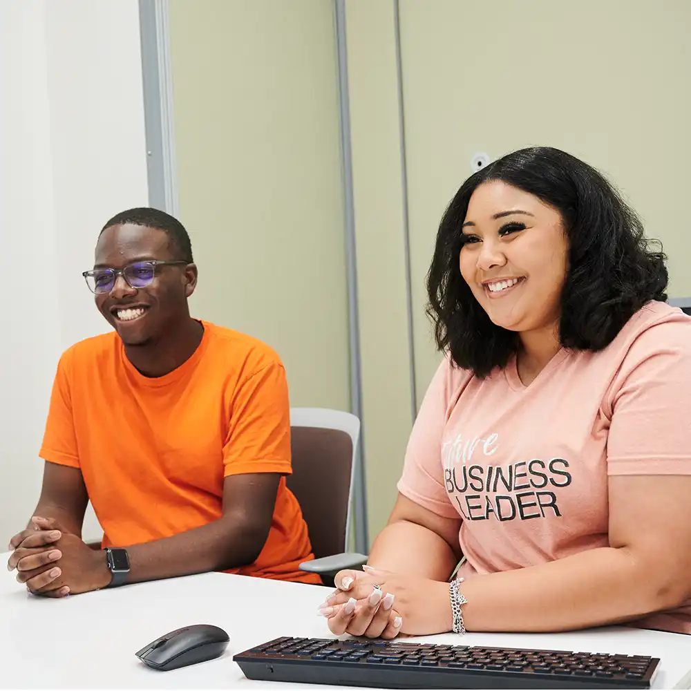 Students at a desk, smiling, about to meet someone.