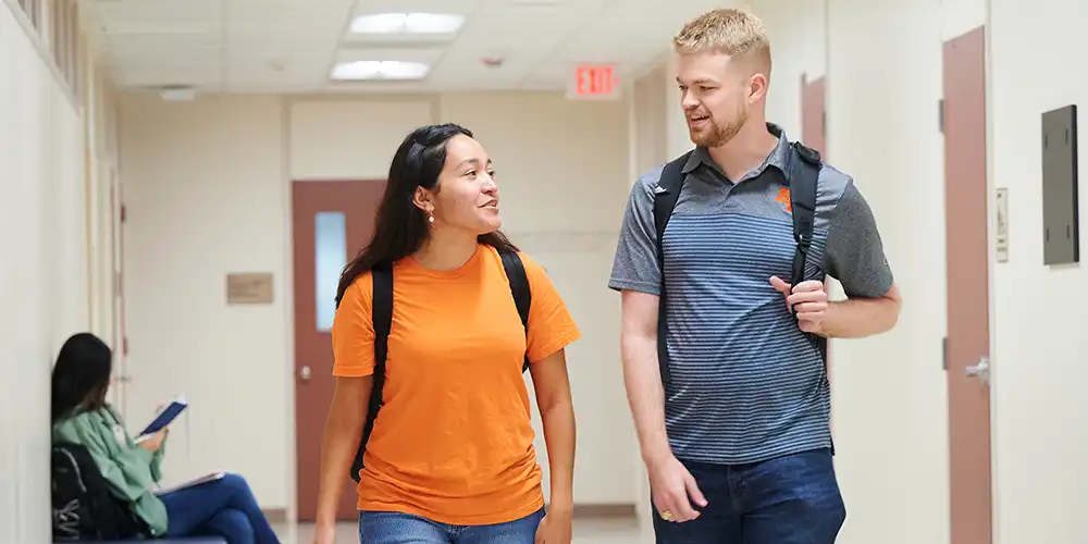 Two students walking through the Smith-Hutson building, while another student reads in the background.
