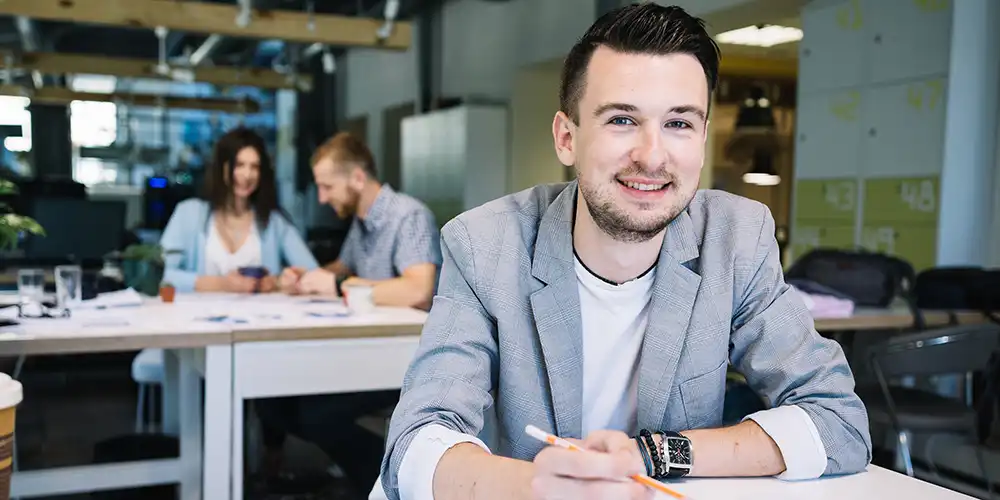 Economics student working and smiling, with another pair working at a table behind him.