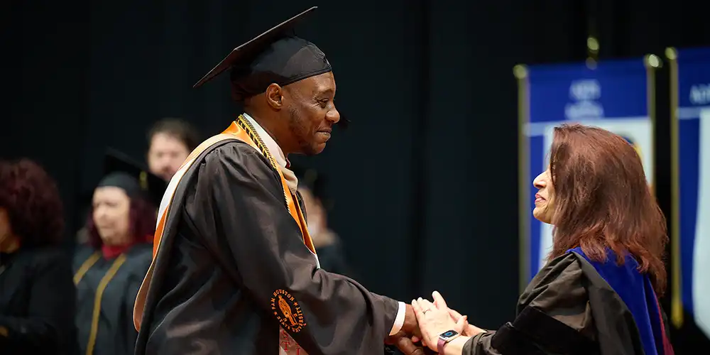 Business student receiving shaking hands with faculty at commencement.