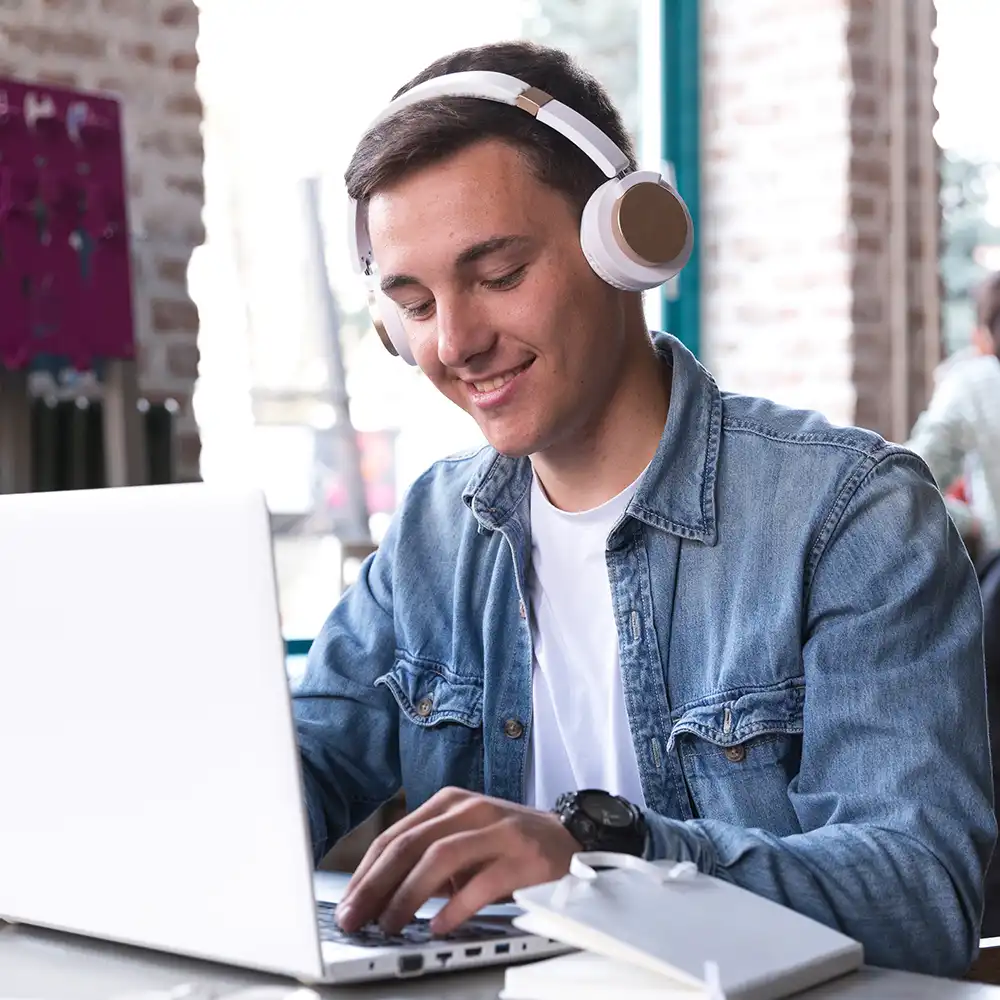 A student working on their laptop while wearing headphones.