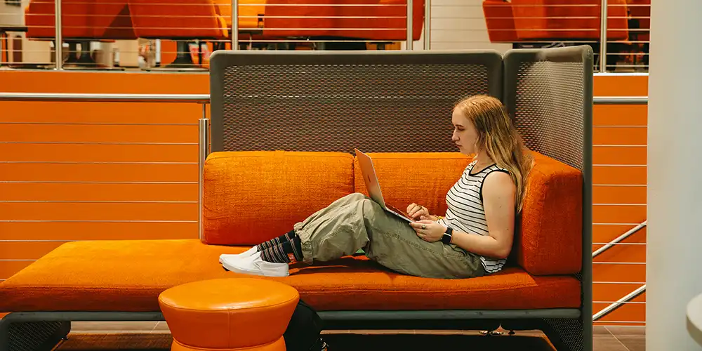 Student sitting on a couch, working on their laptop.