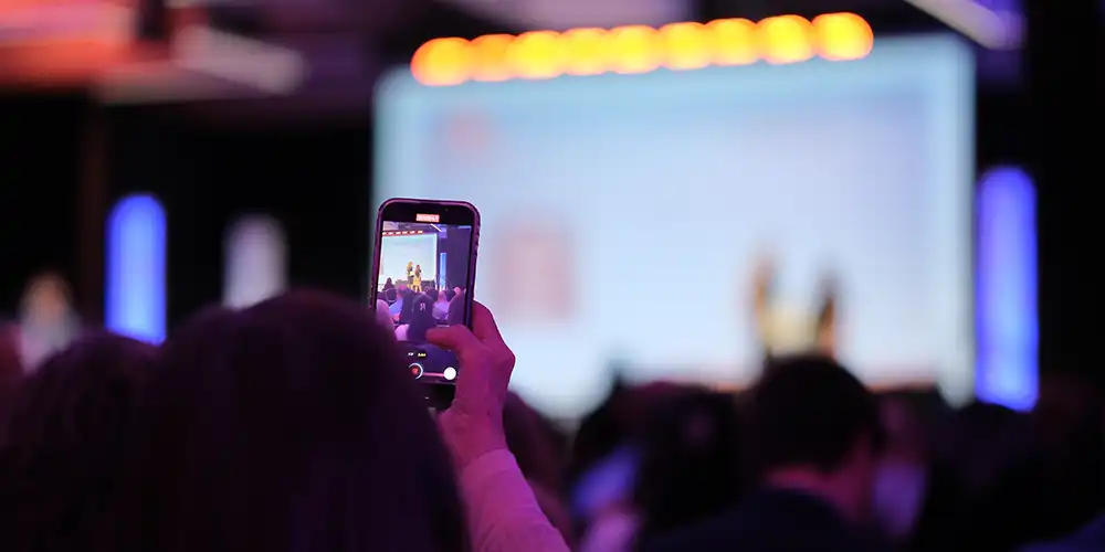 An audience member at a COBA scholarship ceremony taking a photo of the stage with their phone.