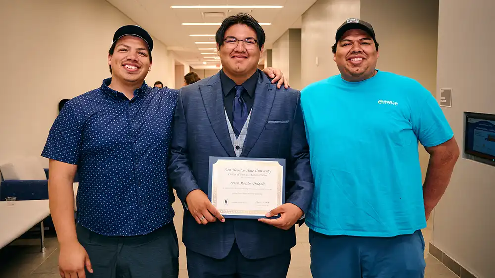 Brian Morales-Delgado holding his scholarship award with two of his family members on both his left and right.