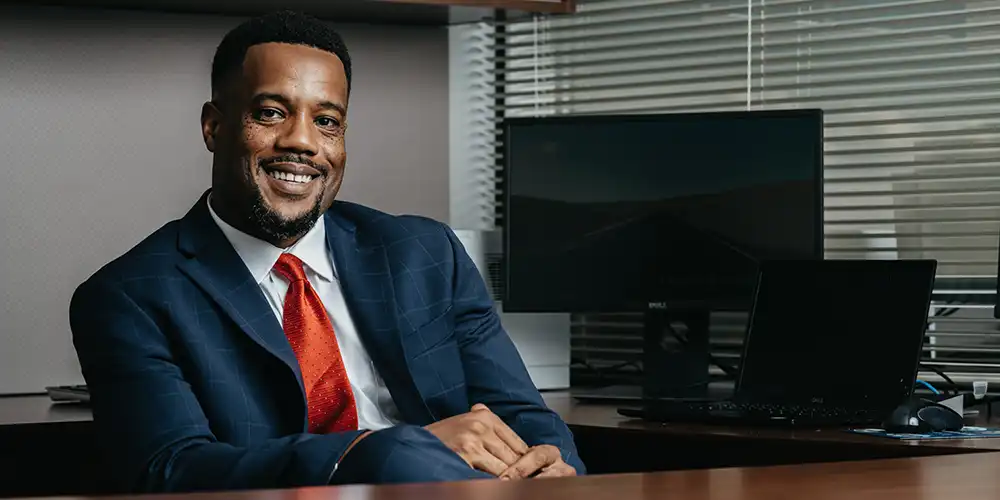 A man sitting at a desk with his leg up, smiling.