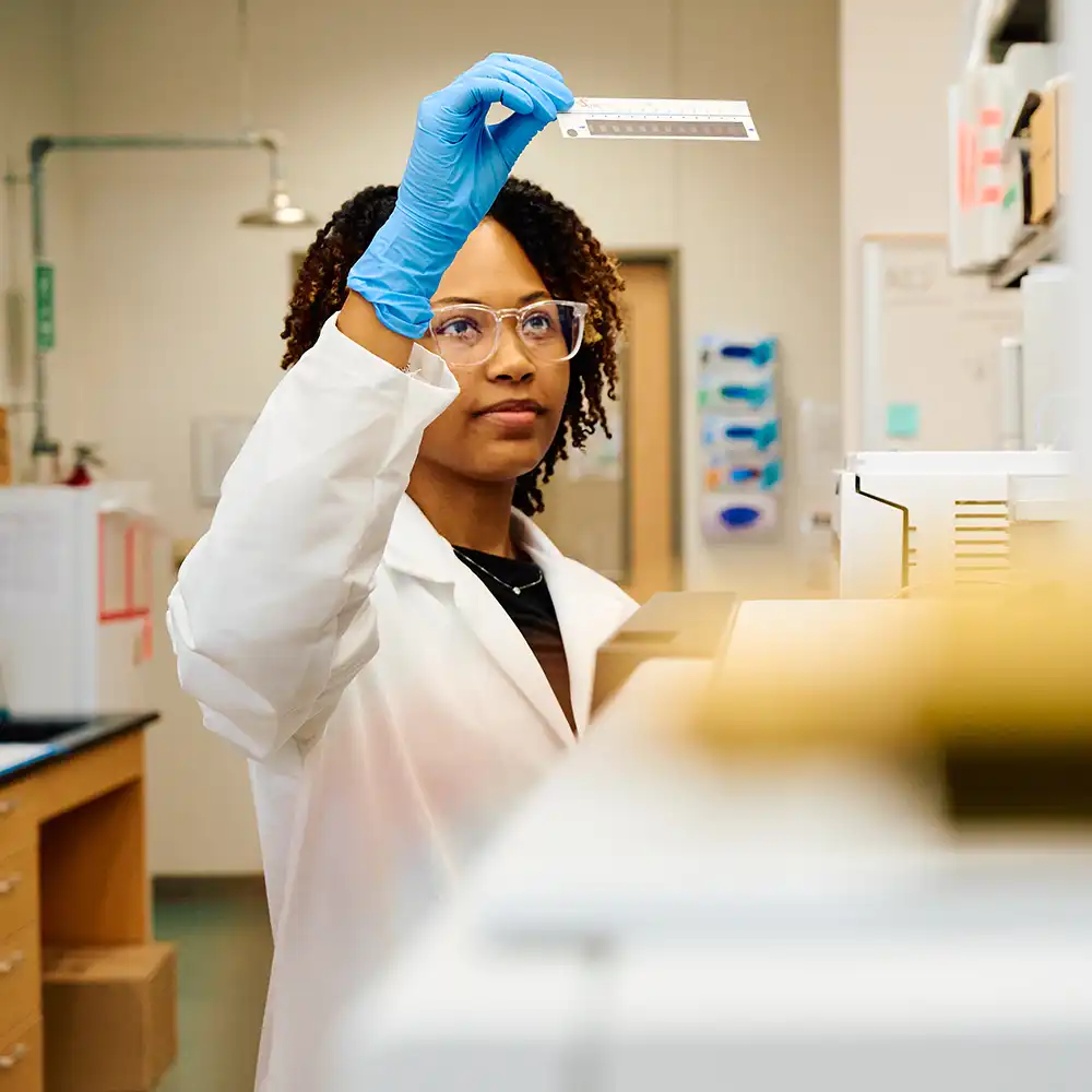 Forensic science student in lab examining a test strip that she is holding up with her hand.