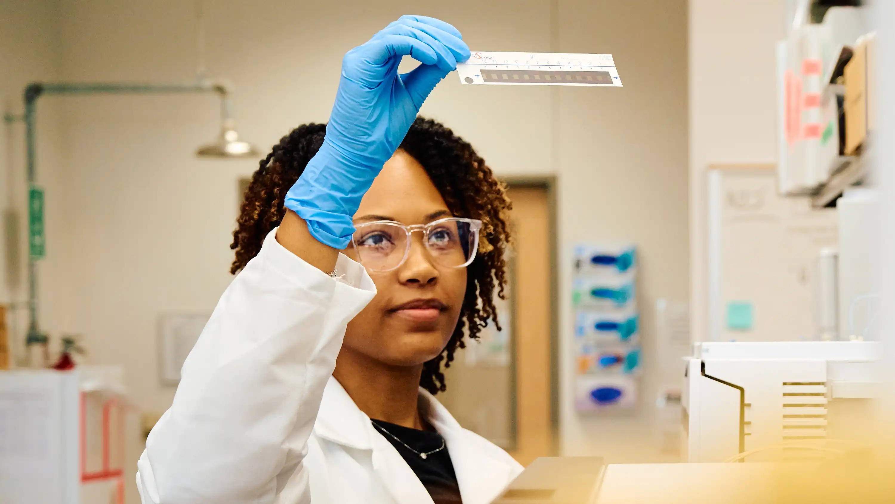 Forensic science student in lab examining a test strip that she is holding up with her hand.