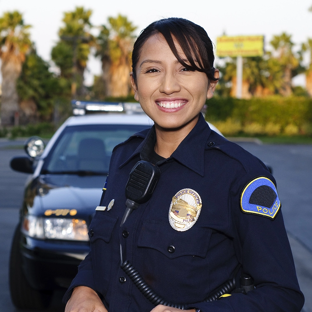 Smiling woman in police uniform in front of police car in background