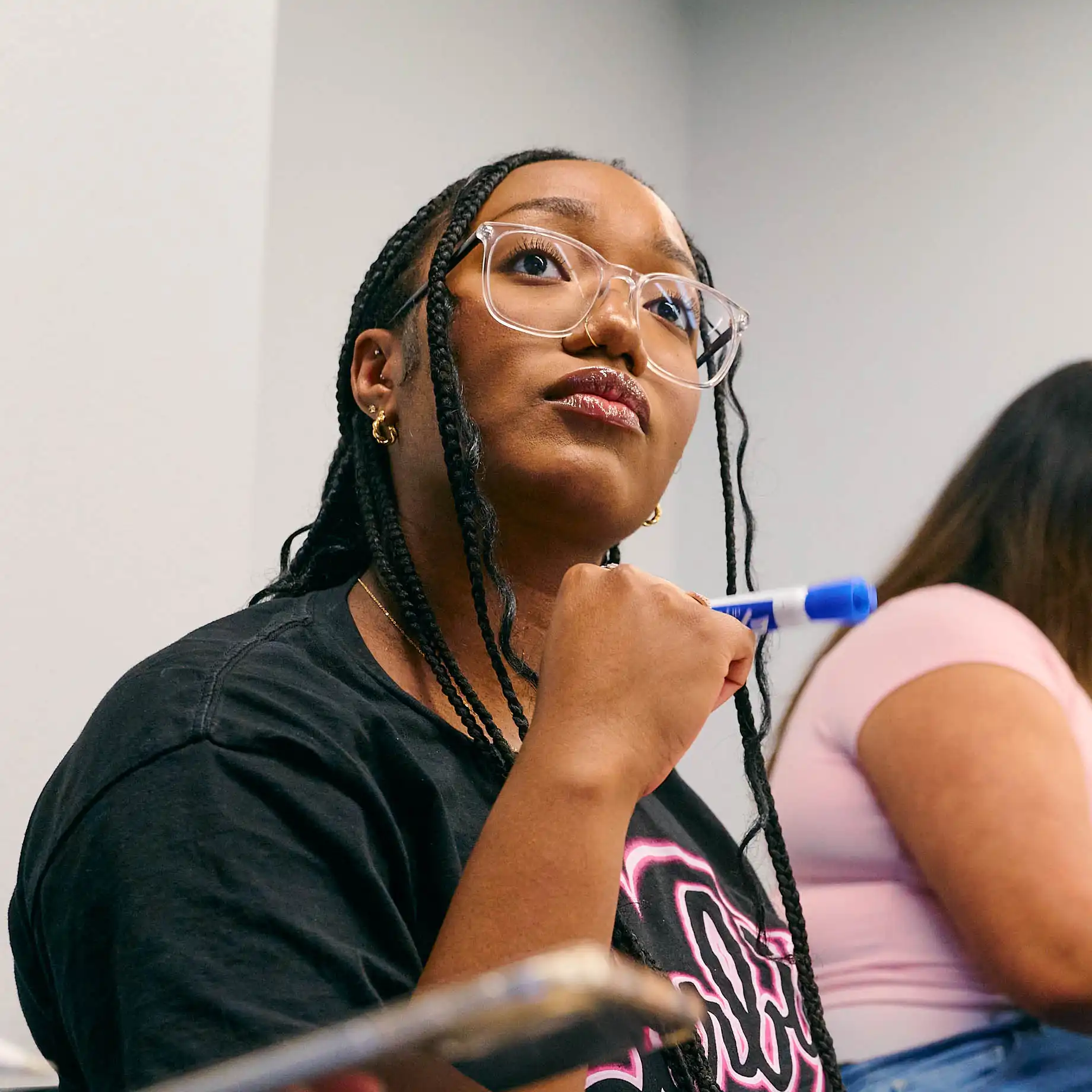 Student in class, holding marker, looking toward front of classroom.