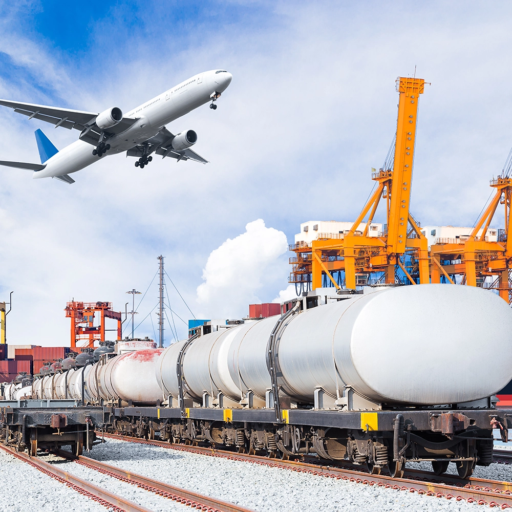 Airplane in sky over tank cars on railroad in front of shipping port machinery and shipping containers in background