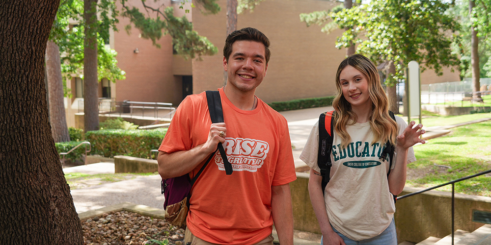 Male college student and female college student smiling for photo outside of a brown brick building