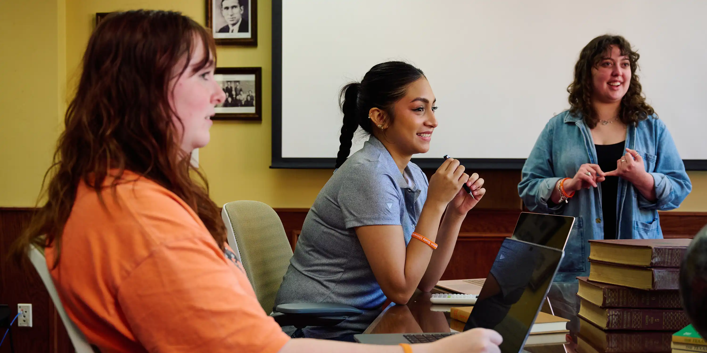 SHSU students sit around a table discussing an assignment with books and laptops.