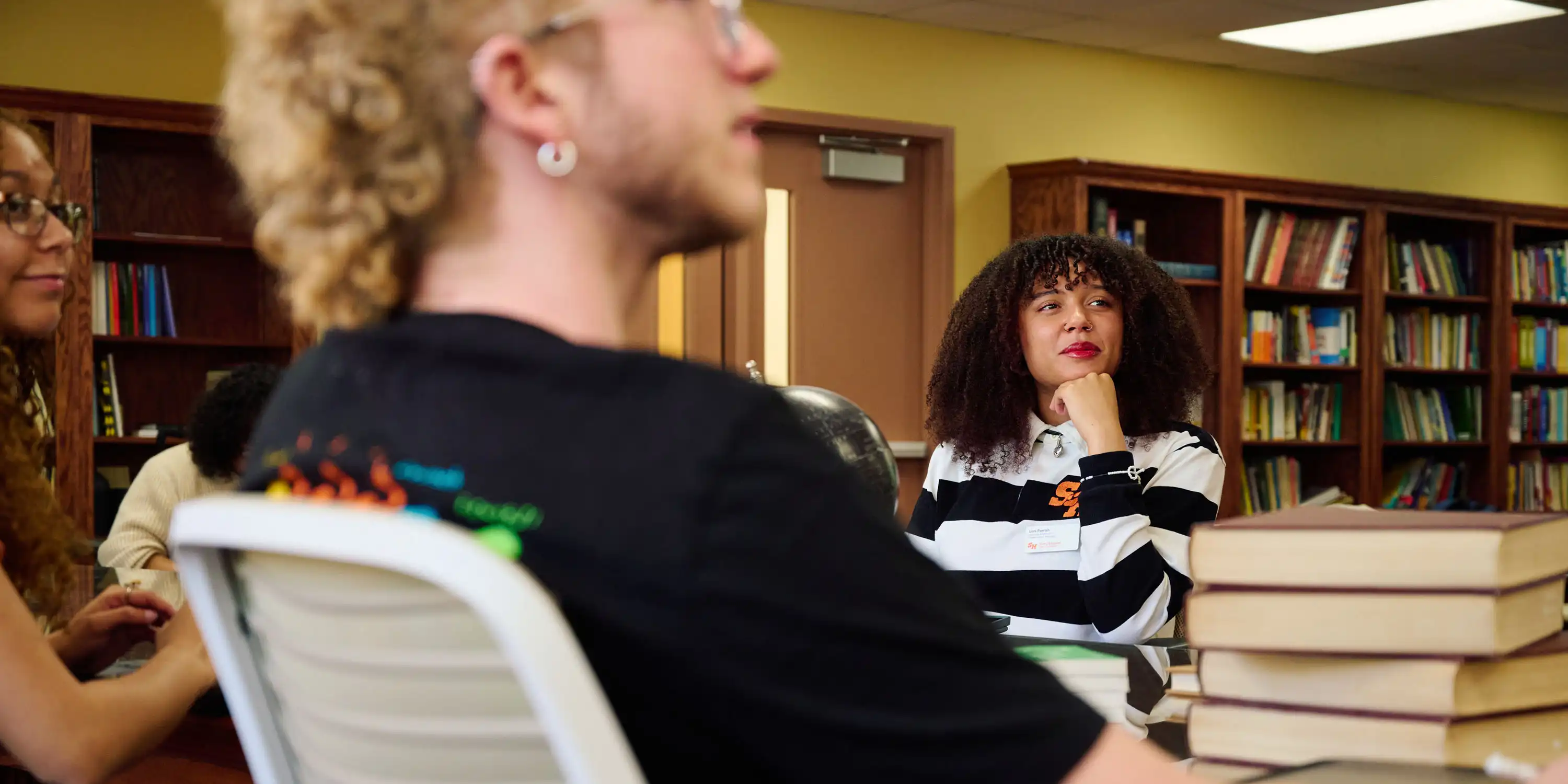 An SHSU student has her hand tucked up under her chin and a small smile on her face as she listens to a fellow student speak.