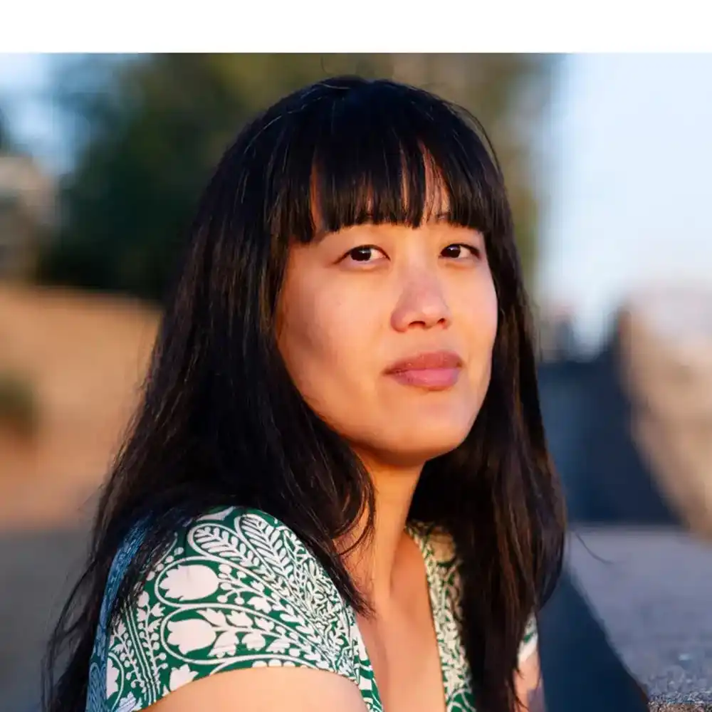 Esther looks at the camera in a white and green floral print top. 