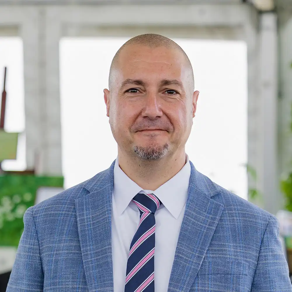 Giuseppe smiles at the camera in a blue suit and pink stripped tie.