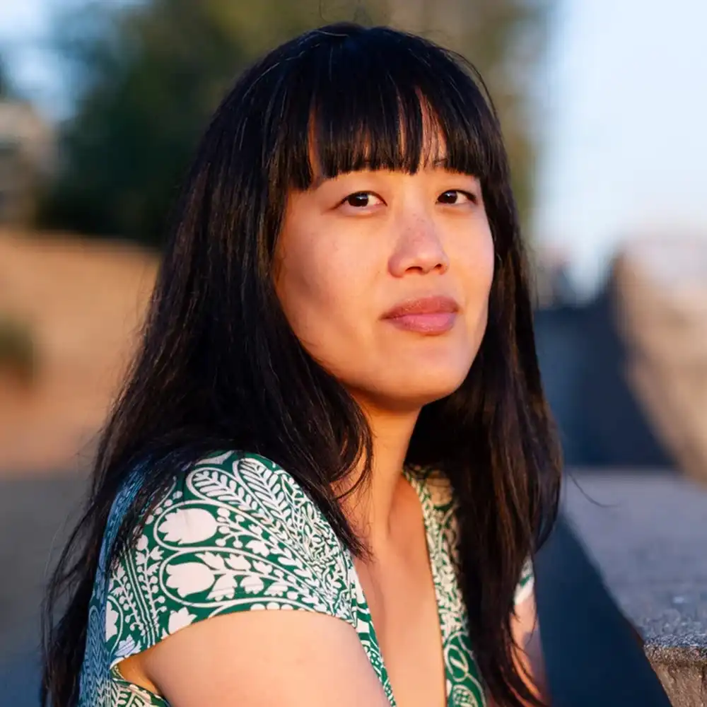 Esther looks at the camera in a white and green floral print top. 