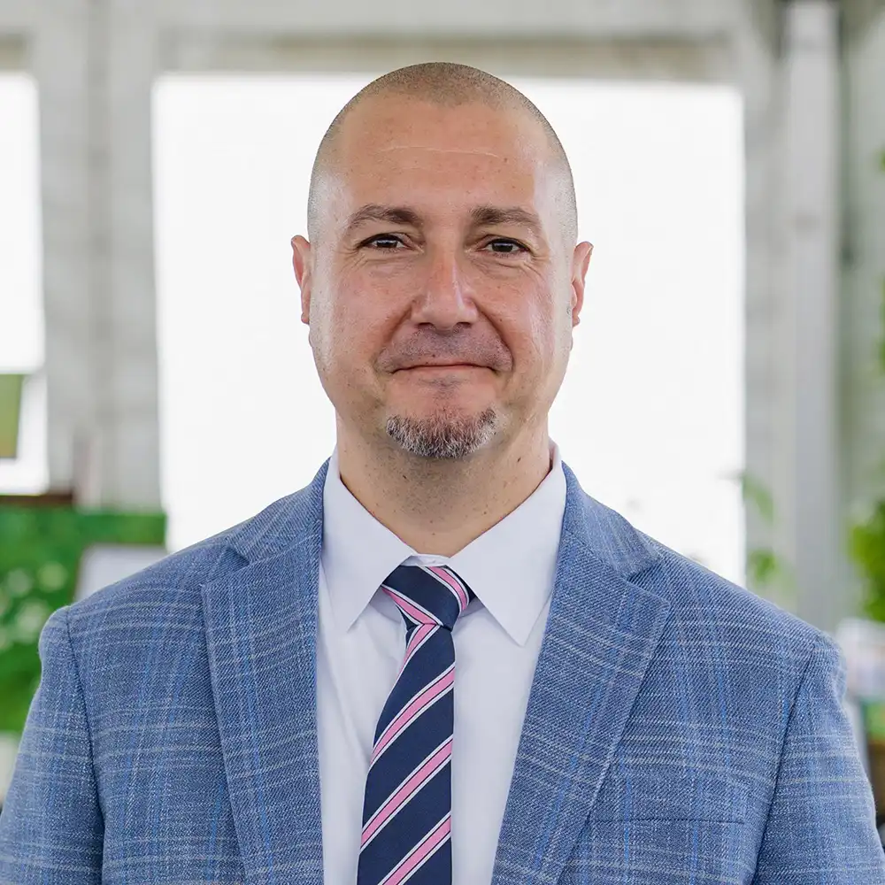 Giuseppe smiles at the camera in a blue suit and pink stripped tie.