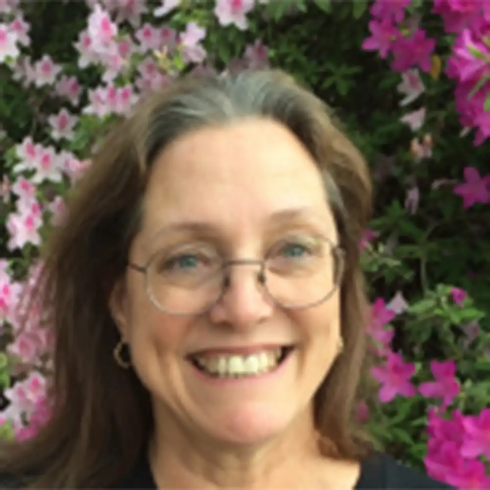 Kim smiles at the camera, surrounded by flowers and bushes.
