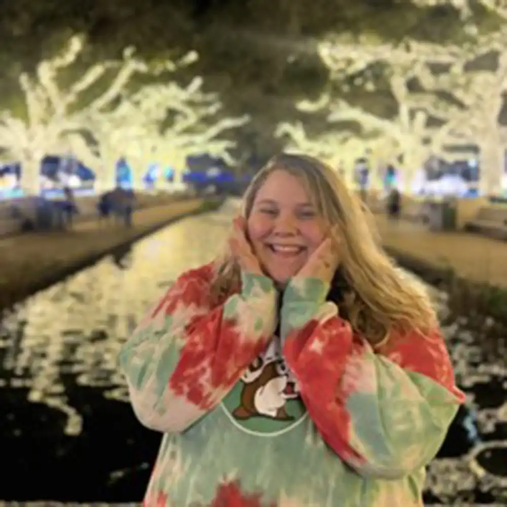 Britt poses outside surrounded by lights with her hands to each side of her face, smiling.