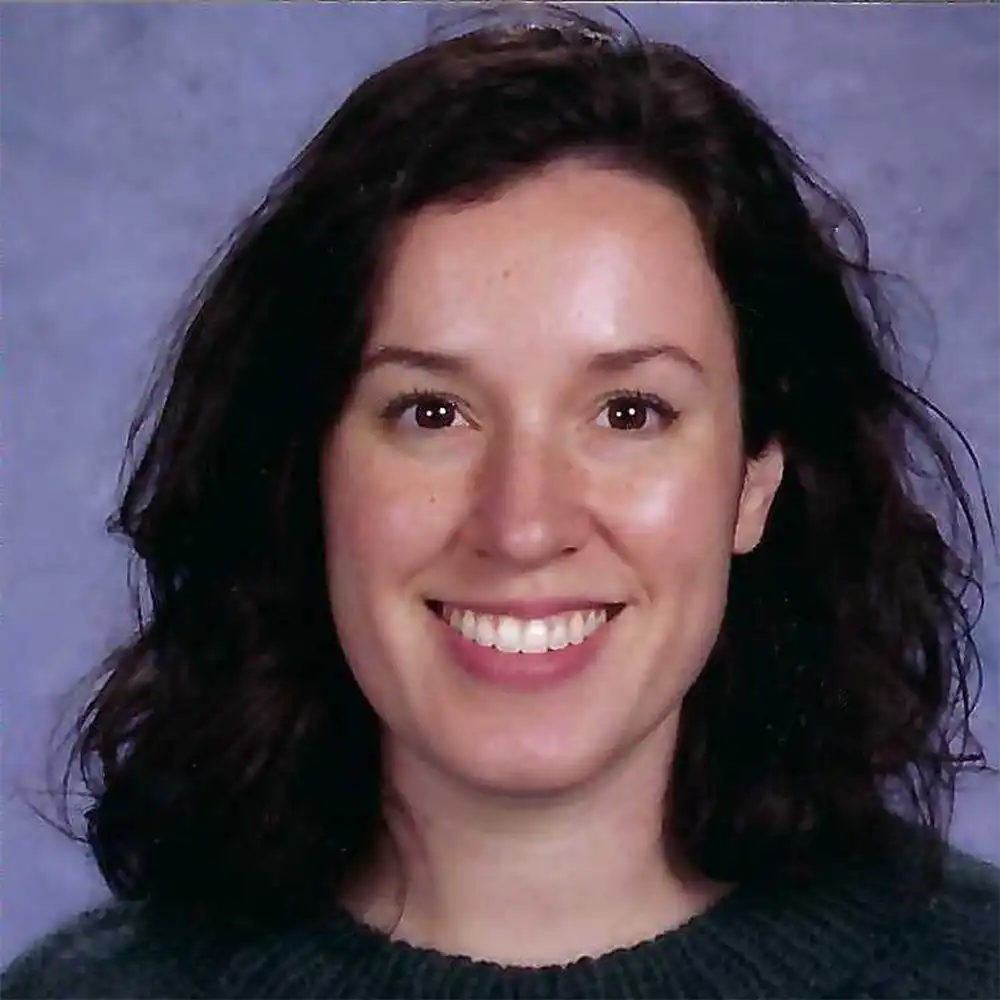 Kayleigh smiles at the camera, face surrounded by long, dark hair and a purple-blue background.