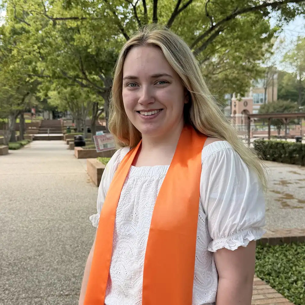 Loren poses on campus with a big smile and graduation outfit.