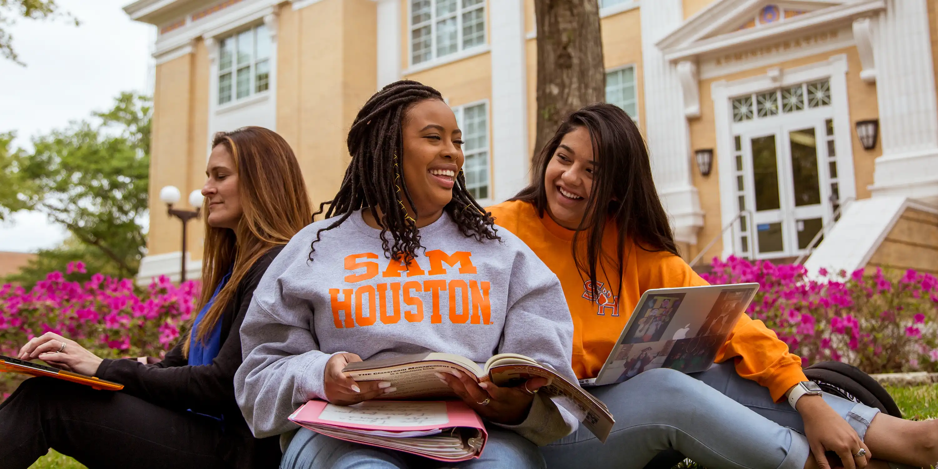 Three SHSU students laugh as they sit outside on campus studying.