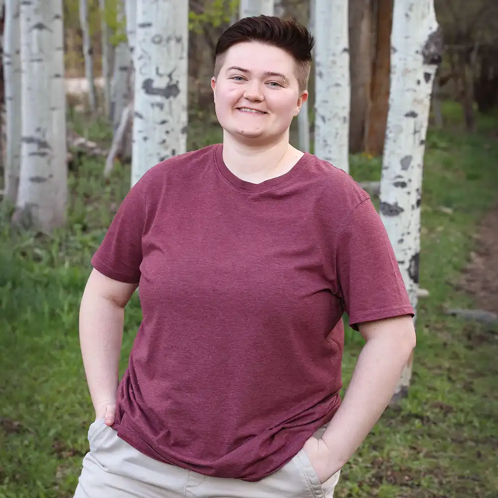 Lindsey stands in a wooded area, wearing a red shirt, and smiling at the camera.