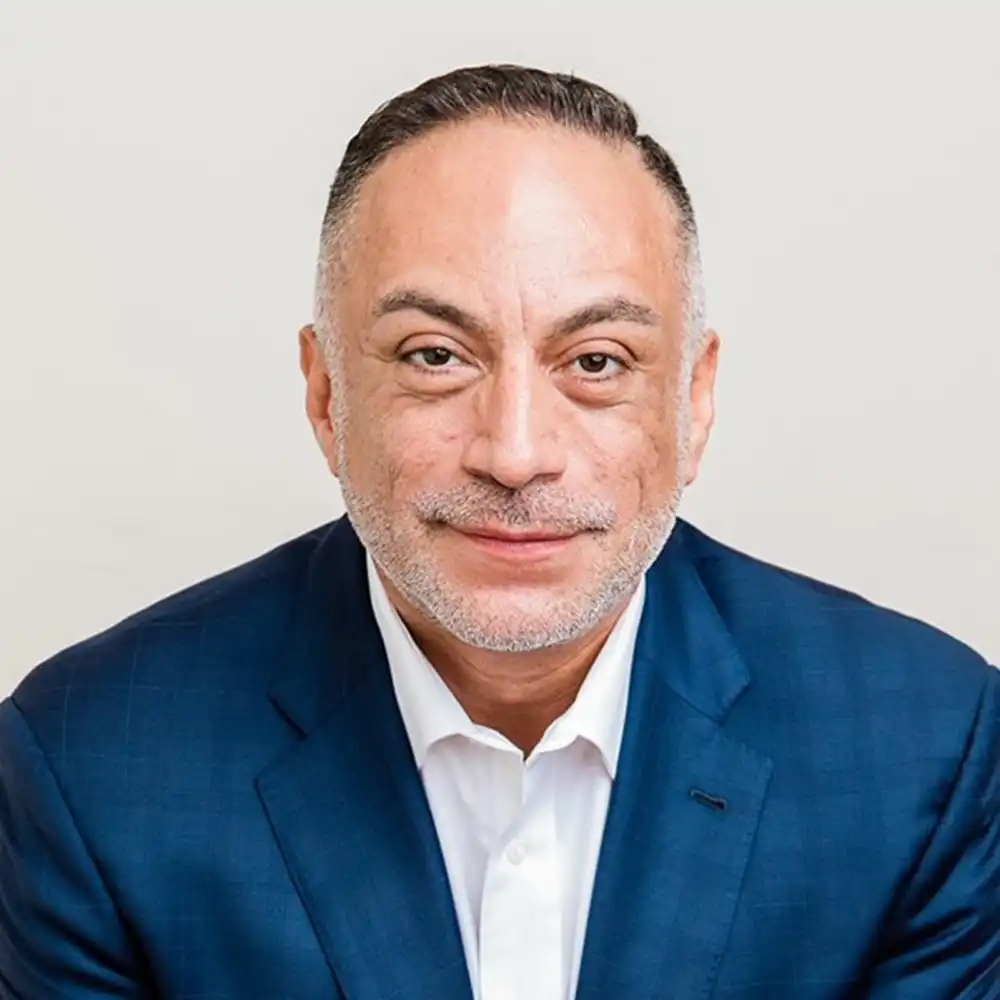 Francisco grins at the camera in a dark blue suit and white button up shirt.