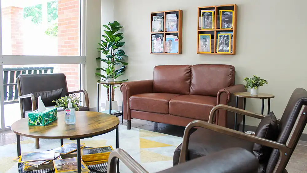 The waiting room of the Psychological Services Center showing comfortable couches, a coffee table, and magazine by a bright window.