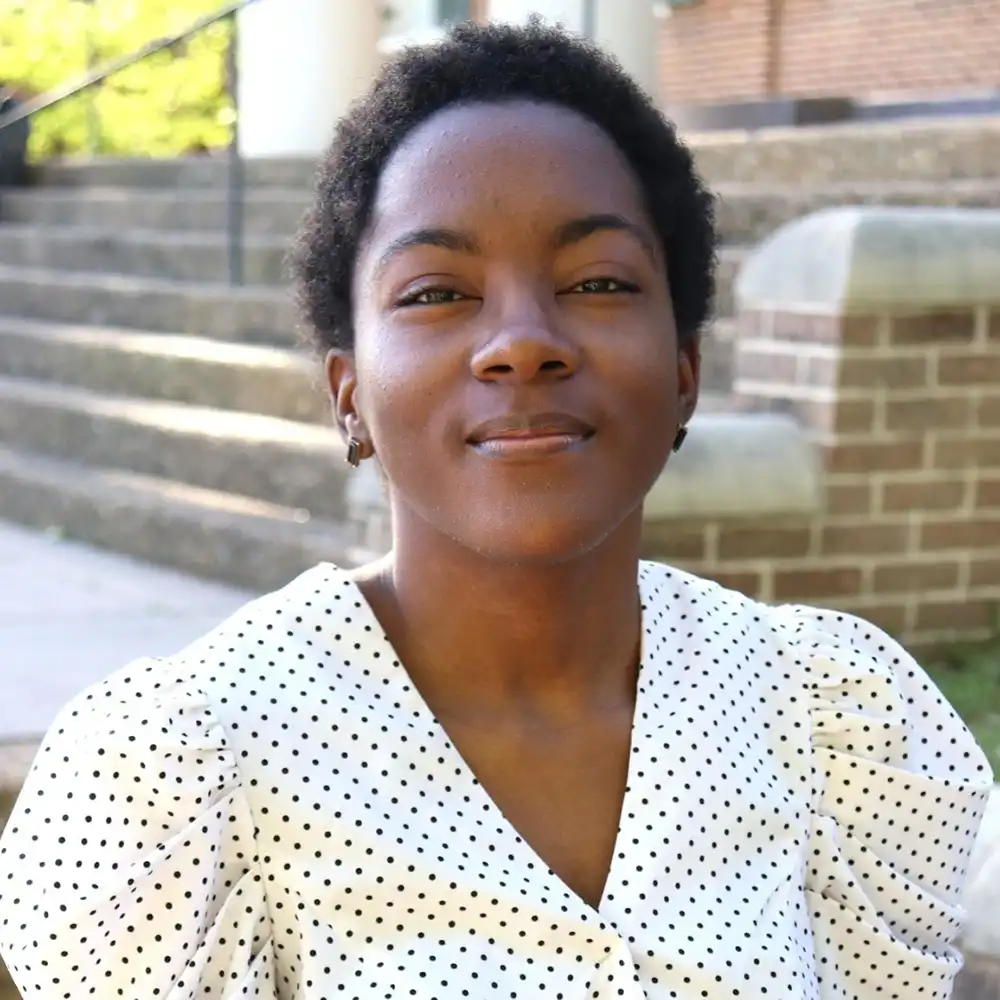 Charise smiles at the camera sitting outside on campus.