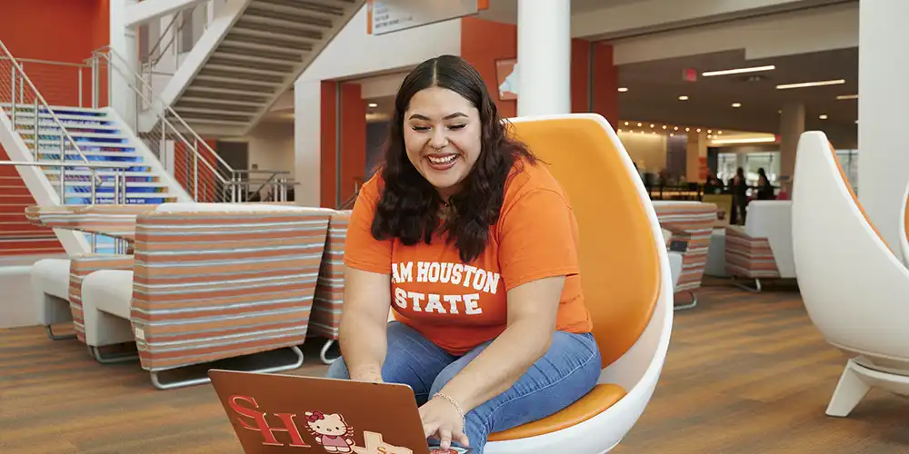SHSU student smiles as she types on her laptop in the Lowman Student Center.