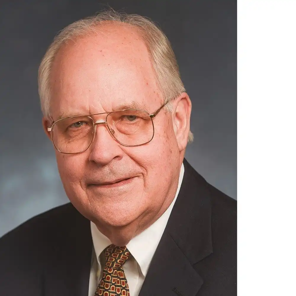 Grinning older white man in glasses and a suit.