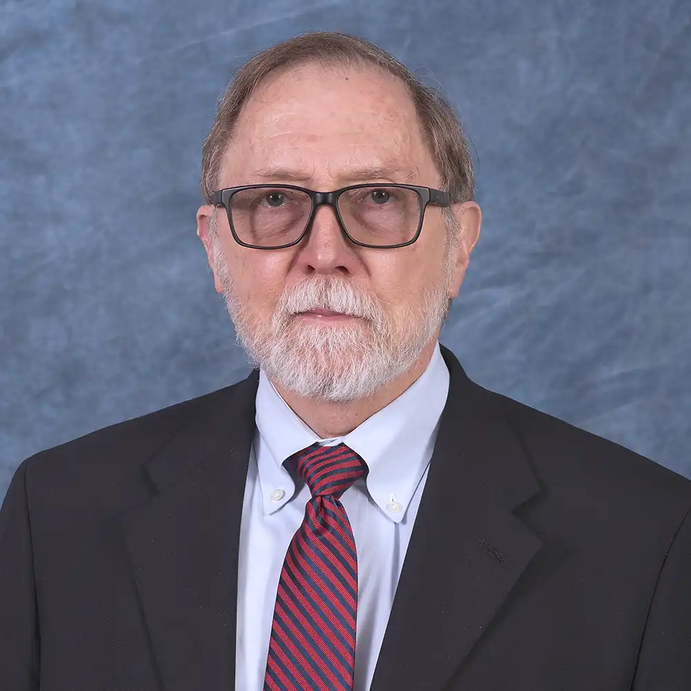Older white man poses in a suit and red tie.
