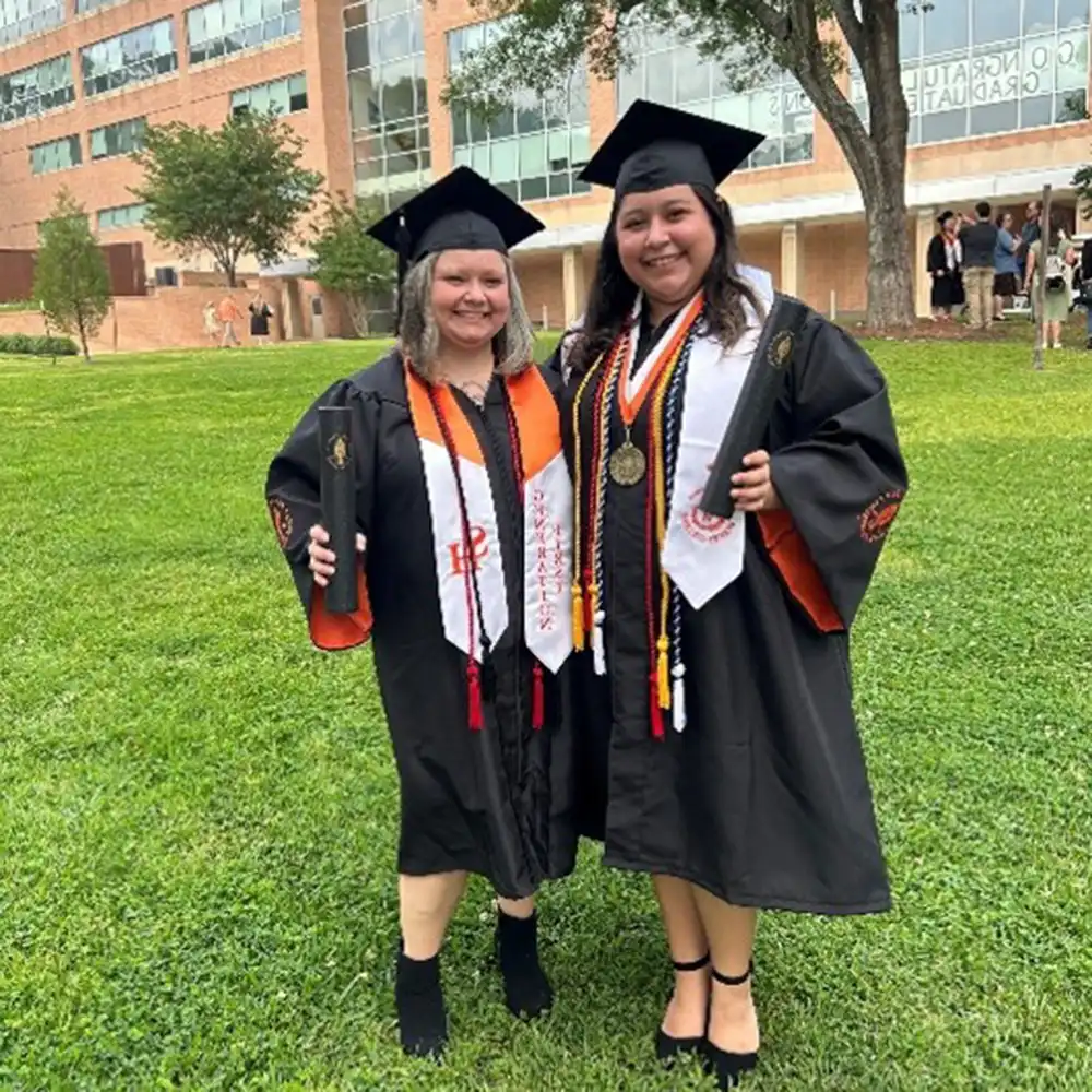 Alyssa poses on campus with a classmate in their graduation outfits.