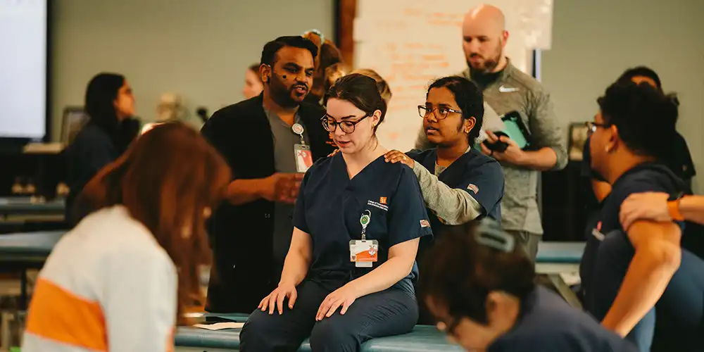 Student practicing OMT techniques with instructor guidance while other students observe