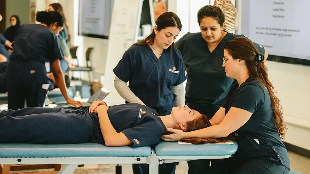 Student laying on treatment table while table trainer explains techniques and two additional students observe