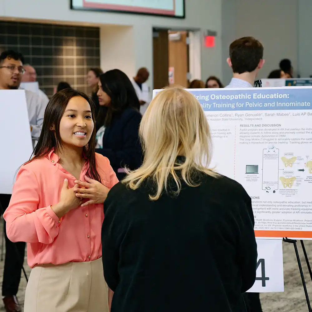 Student presenting research poster to SHSU-COM staff member