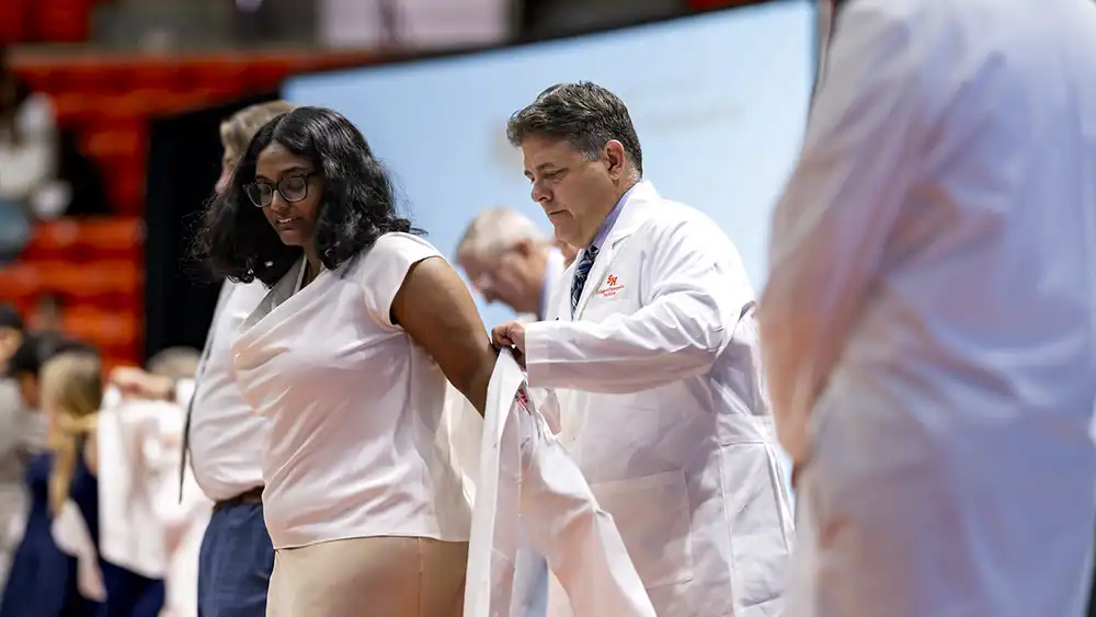 Dr. Langley putting a white coat on a student doctor