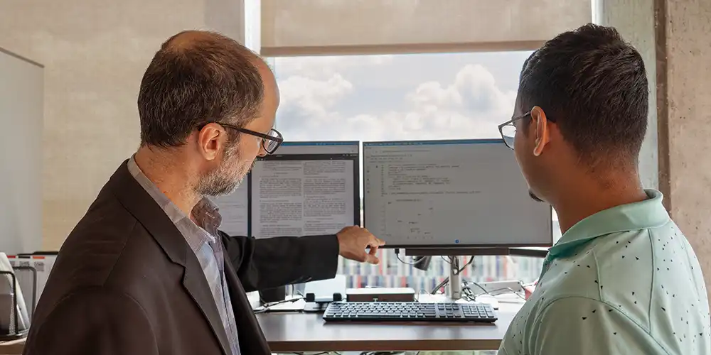Faculty member and student looking at computer screens while faculty member is teaching student