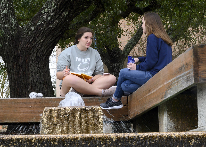 Two college students talk and study by the fountain on campus.