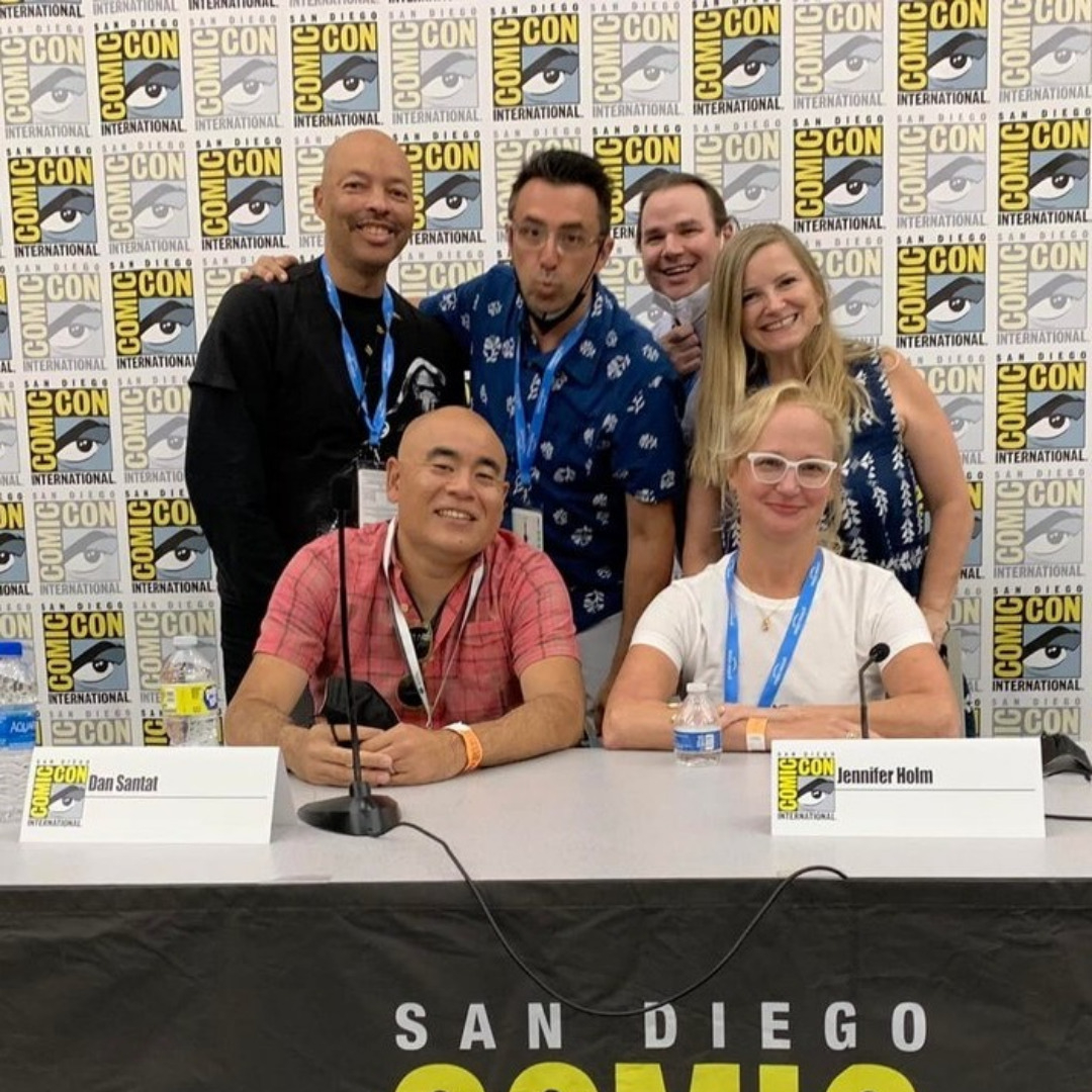 A group of people posing for a photo behind a table at San Diego Comic Con