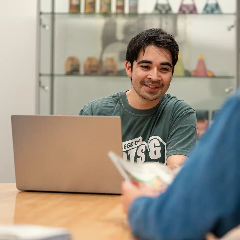 Two women looking at each other, smiling, sitting down, working on an assignment.
